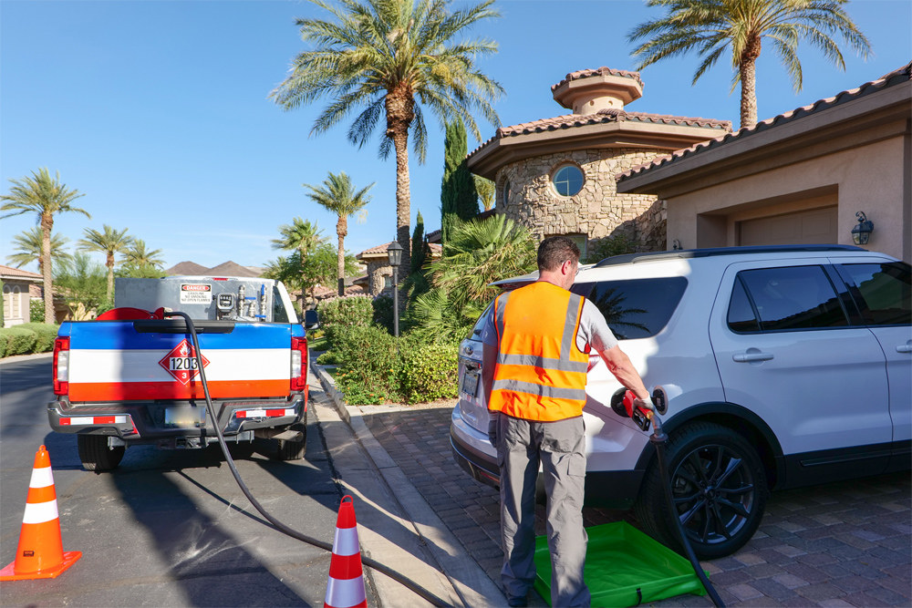 A fuel delivery technician in a hi-vis vest refuels a customer&rsquo;s SUV in a driveway from a fuel skid mounted in a pickup truck.